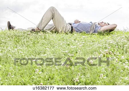 Full length of young man lying on grass against sky View Large Photo Image Stock Photo - Full length of young man lying on grass against sky. Fotosearch
