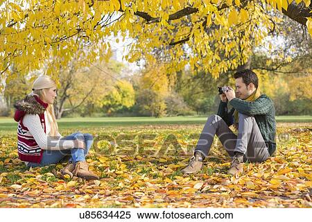 Full length of young man photographing woman in park during autumn View Large Photo Image Stock Photography - Full length of young man photographing woman in park during autumn. Fotosearch