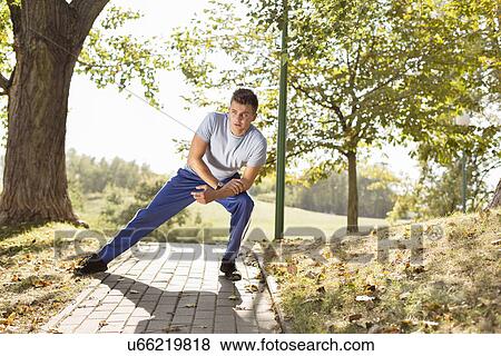 Full length of young man stretching on path in park View Large Photo Image Stock Photo - Full length of young man stretching on path in park. Fotosearch