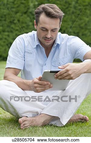 Full length of young man using digital tablet in park View Large Photo Image Picture - Full length of young man using digital tablet in park. Fotosearch