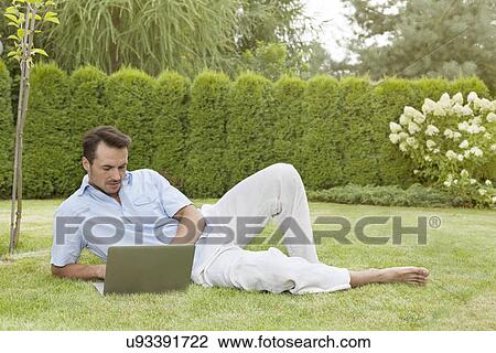 Full length of young man using laptop while reclining in park View Large Photo Image Stock Image - Full length of young man using laptop while reclining in park. Fotosearch