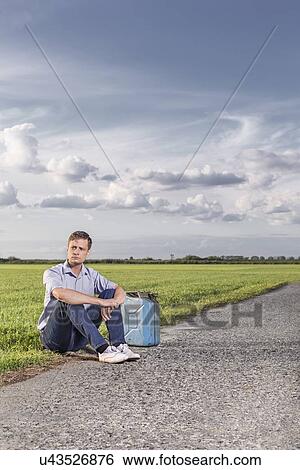 Full length of young man with empty petrol can sitting by country road View Large Photo Image Stock Photograph - Full length of young man with empty petrol can sitting by country road. Fotosearch