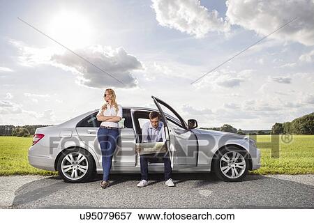 Full length of young woman looking away while man reading map in car at countryside View Large Photo Image Stock Photo - Full length of young woman looking away while man reading map in car at countryside. Fotosearch
