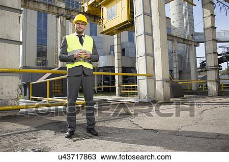 Stock Image - Full length portrait of confident young male architect standing outside industry. Fotosearch