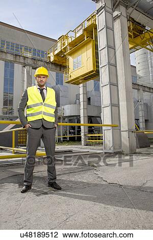Stock Image - Full length portrait of confident young male engineer standing outside industry. Fotosearch
