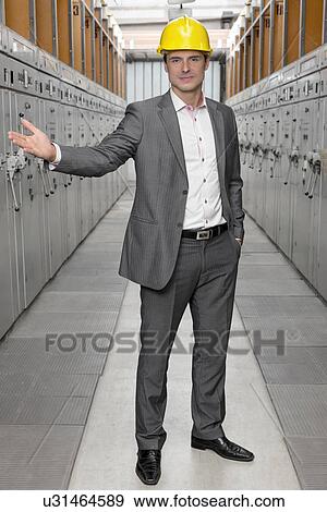 Stock Photo - Full length portrait of confident young male inspector gesturing in control room. Fotosearch