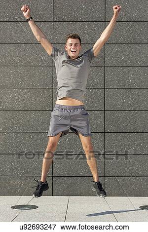 Stock Photo - Full length portrait of excited jogger jumping against tiled wall. Fotosearch