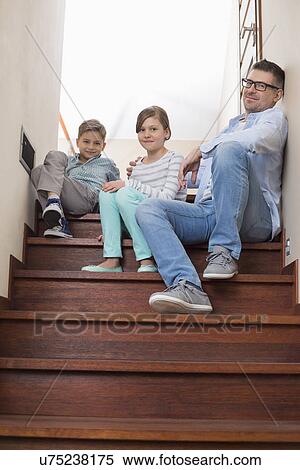 Stock Photography - Full length portrait of father and children sitting on steps at home. Fotosearch