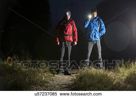 Stock Photography - Full length portrait of male hikers with flashlights in field at night. Fotosearch