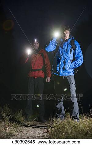 Stock Photography - Full length portrait of male backpackers with flashlights in field at night. Fotosearch