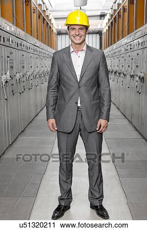 Stock Image - Full length portrait of smiling young male supervisor standing in control room. Fotosearch