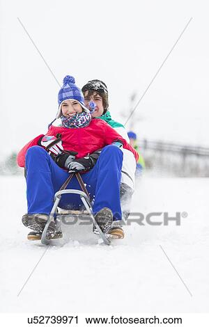 Stock Image - Full length portrait of young couple enjoying sled ride in snow. Fotosearch