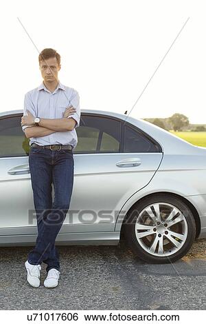 Full length portrait of young man standing by car at countryside View Large Photo Image Stock Photograph - Full length portrait of young man standing by car at countryside. Fotosearch