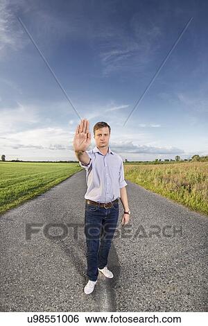 Stock Photograph - Full length portrait of young man making stop gesture at country road. Fotosearch