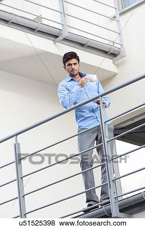Stock Photo - Full length portrait of young businessman having coffee at hotel balcony. Fotosearch