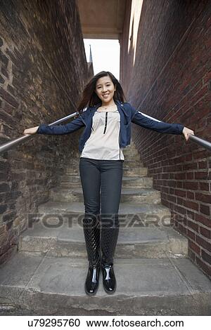 Stock Image - Full length portrait of young woman standing on steps at London, England, UK. Fotosearch