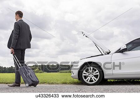 Full length rear view of young businessman with luggage leaving broken down car at countryside View Large Photo Image Stock Image - Full length rear view of young businessman with luggage leaving broken down car at countryside. Fotosearch