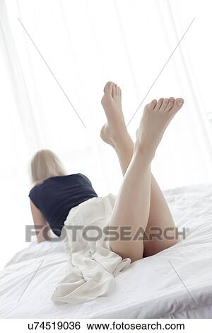 Stock Photograph - Full length rear view of young woman lying in bed. Fotosearch