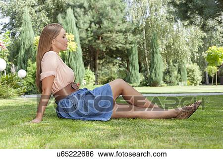 Full length side view of beautiful young woman relaxing on grass in park View Large Photo Image Stock Photograph - Full length side view of beautiful young woman relaxing on grass in park. Fotosearch