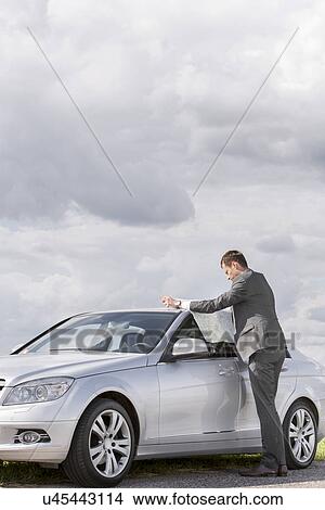 Full length side view of businessman reading map by car at countryside View Large Photo Image Picture - Full length side view of businessman reading map by car at countryside. Fotosearch