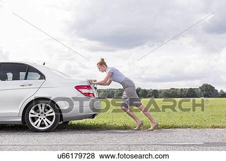 Stock Photo - Full length side view of businesswoman pushing broken down car at countryside. Fotosearch