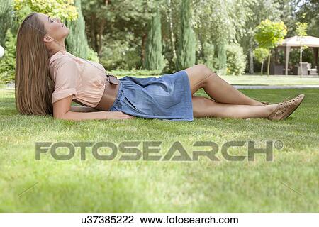 Full length side view of relaxed young woman lying on grass in park View Large Photo Image Stock Image - Full length side view of relaxed young woman lying on grass in park. Fotosearch
