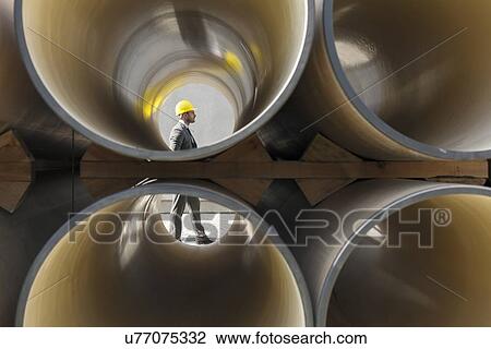 Full length side view of young male architect walking by stacked pipes at construction site View Large Photo Image Stock Image - Full length side view of young male architect walking by stacked pipes at construction site. Fotosearch