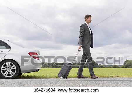 Full length side view of young businessman with suitcase leaving broken down car at countryside View Large Photo Image Picture - Full length side view of young businessman with suitcase leaving broken down car at countryside. Fotosearch