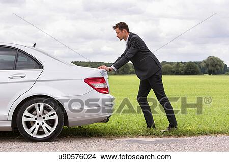 Full length side view of young businessman pushing broken down car at countryside View Large Photo Image Picture - Full length side view of young businessman pushing broken down car at countryside. Fotosearch