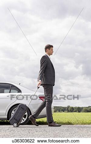 Full length side view of young businessman with luggage walking by broken down car at countryside View Large Photo Image Stock Image - Full length side view of young businessman with luggage walking by broken down car at countryside. Fotosearch