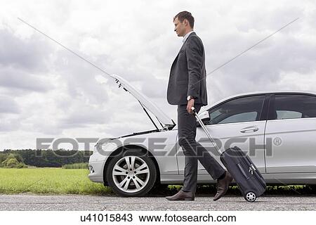 Full length side view of young businessman with luggage walking by broken down car at countryside View Large Photo Image Stock Image - Full length side view of young businessman with luggage walking by broken down car at countryside. Fotosearch
