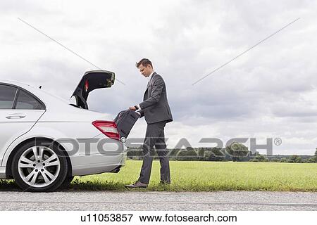 Full length side view of young businessman unloading luggage from broken down car at countryside View Large Photo Image Stock Photo - Full length side view of young businessman unloading luggage from broken down car at countryside. Fotosearch