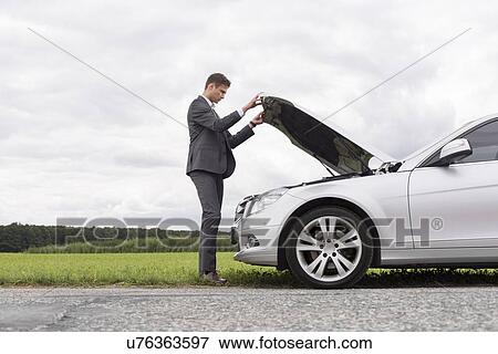 Full length side view of young businessman opening broken down car hood at countryside View Large Photo Image Stock Photo - Full length side view of young businessman opening broken down car hood at countryside. Fotosearch