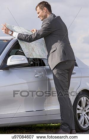 Full length side view of young businessman reading map by car at countryside View Large Photo Image Stock Photo - Full length side view of young businessman reading map by car at countryside. Fotosearch