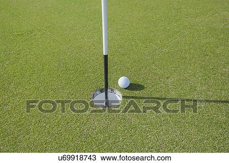 Stock Image - Golf ball at edge of hole. Fotosearch