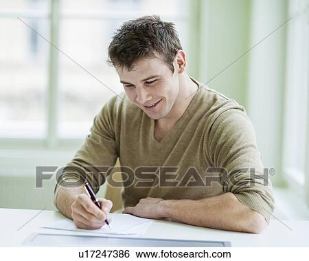 Handsome businessman writing on document at desk in office View Large Photo Image Stock Photograph - Handsome businessman writing on document at desk in office. Fotosearch
