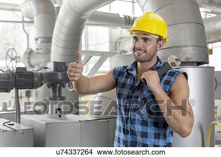 Handsome manual worker gesturing thumbs up in industry View Large Photo Image Picture - Handsome manual worker gesturing thumbs up in industry. Fotosearch