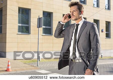Stock Image - Handsome young businessman using cell phone outdoors. Fotosearch