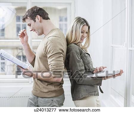 Stock Photo - Happy business couple holding book and laptop in office. Fotosearch