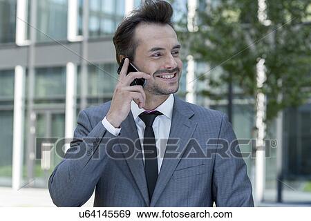 Stock Photo - Happy businessman conversing on cell phone outside office. Fotosearch