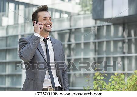 Happy businessman using cell phone outside office View Large Photo Image Stock Photograph - Happy businessman using cell phone outside office. Fotosearch