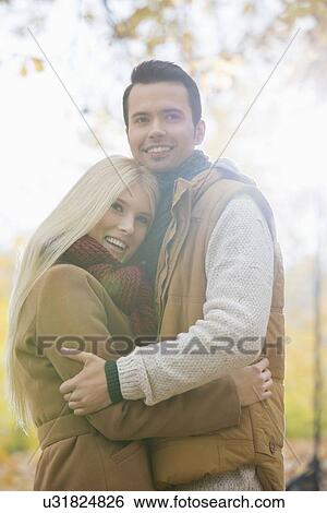 Happy couple in jackets hugging in park View Large Photo Image Stock Photograph - Happy couple in jackets hugging in park. Fotosearch