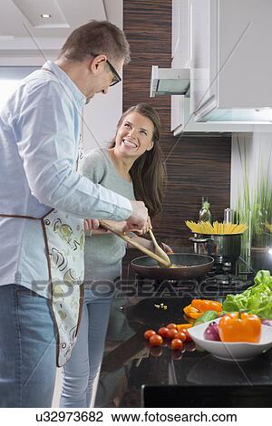 Stock Image - Happy couple preparing food in kitchen. Fotosearch