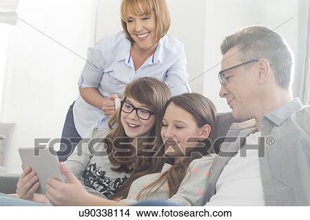 Picture - Happy family using tablet PC on sofa at home. Fotosearch