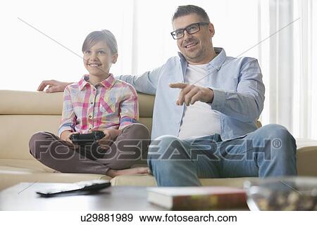 Stock Photo - Happy father and daughter playing video game in living room. Fotosearch