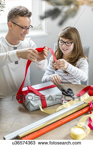 Stock Image - Happy father and daughter wrapping Christmas present at home. Fotosearch