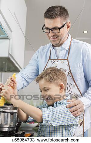 Stock Image - Happy father and son preparing spaghetti together in kitchen. Fotosearch