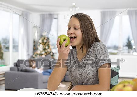 Stock Image - Happy girl eating apple at home. Fotosearch