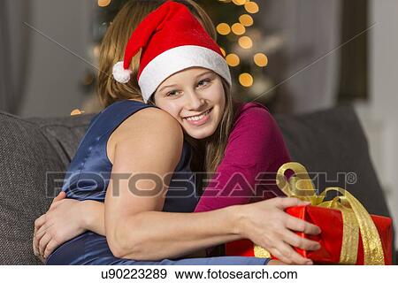 Stock Photo - Happy girl hugging mother during Christmas at home. Fotosearch