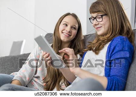 Happy girl looking at sister using digital tablet on sofa at home View Large Photo Image Stock Photograph - Happy girl looking at sister using digital tablet on sofa at home. Fotosearch